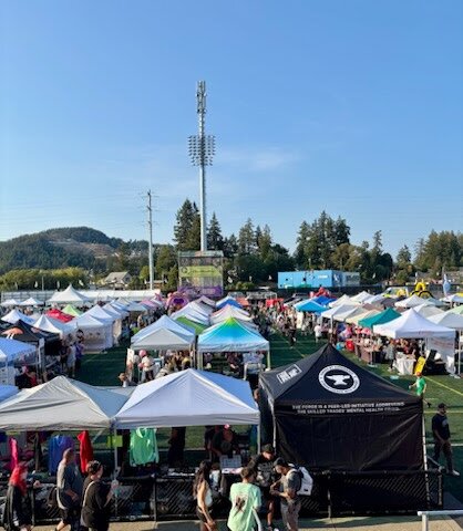 Rows of vendor tents on the field at SoberFest Victoria, with hills behind